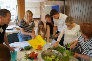 Zu sehen sind sieben Personen, die um einen Tisch herum stehen und gemeinsam einen Salat vorbereiten. Aufgenommen wurde das Bild im Rahmen der Nachbarschaftsgespräche in Ludwigsburg.