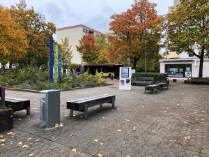 Zu sehen ist ein öffentlicher Platz, auf dem mehrere Bänke angebracht wurden. Im Hintergrund sieht man einen Bus, der auf einer Straße fährt. Auf dem Platz ist eine kleine Grünfläche sichtbar, auf der verschiedene Pflanzen angebracht wurden. Aufgenommen wurde das Bild im Rahmen der Nachbarschaftsgespräche in Heilbronn.